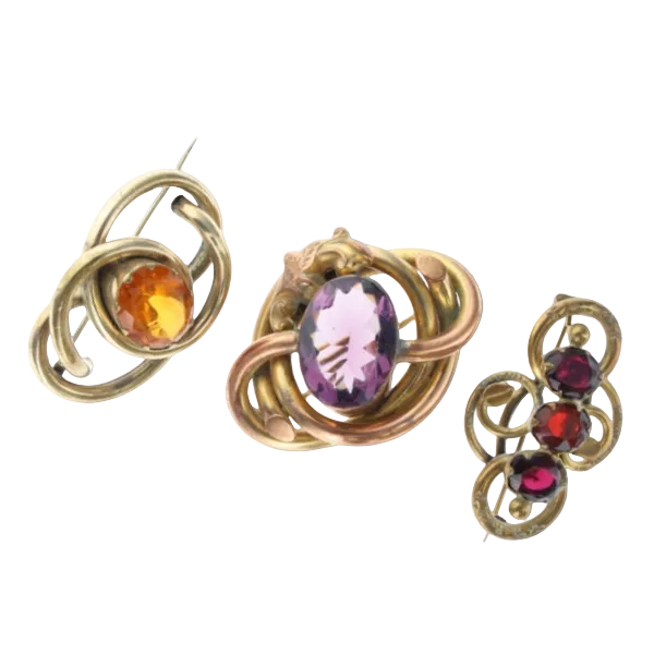 Three vintage gold-toned brooches with oval gemstones in amber, purple, and red, displayed on a light gray background.